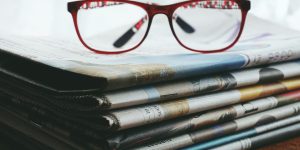 pexels-photo-3886870-3886870 Red eyeglasses resting on a stack of newspapers symbolize reading and information.